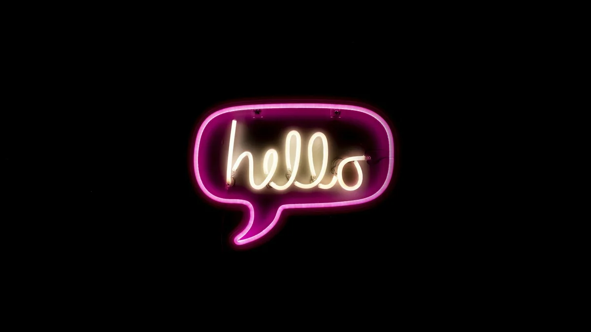 Siyah zeminde pembe neon ışıkla yazılmış, konuşma balonu içinde "hello" yazısı