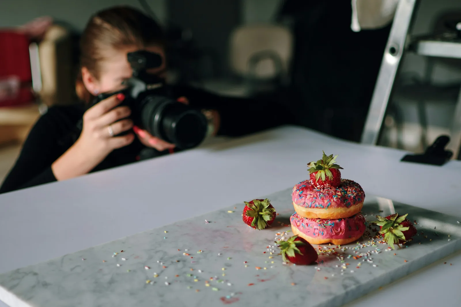Mermer bir tezgahta çilekli donutların fotoğrafını çeken bir fotoğrafçı