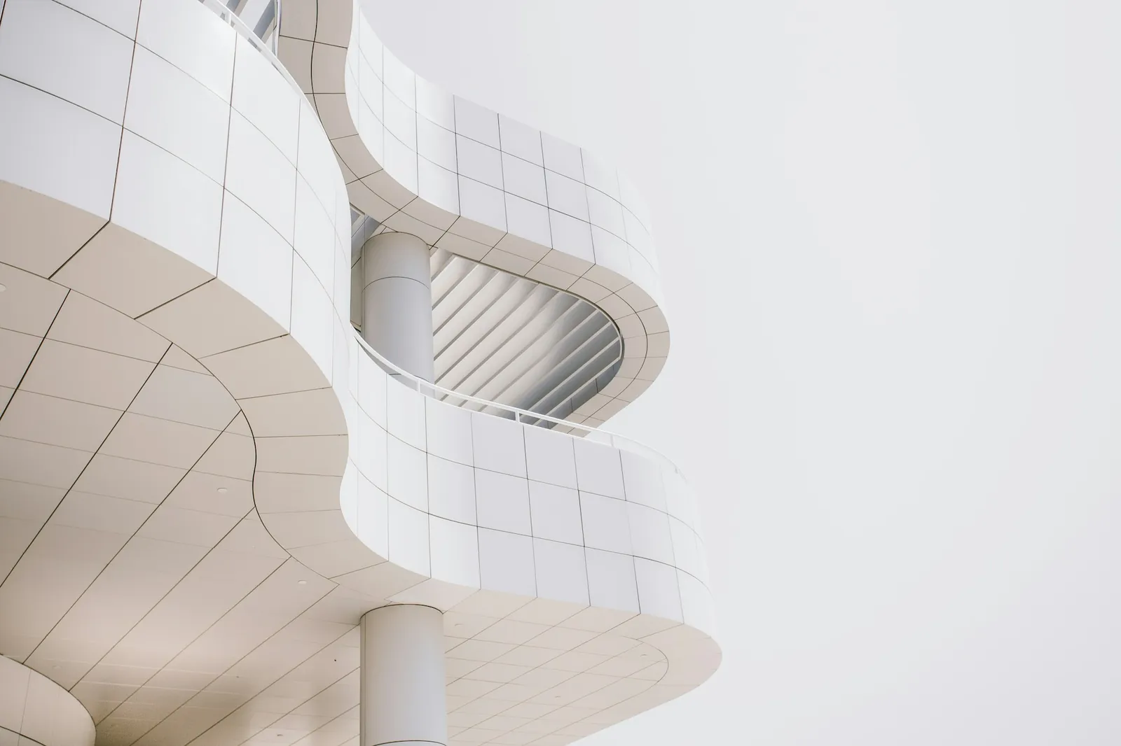 Açık gri gökyüzü önünde beyaz panellerle kaplı, kıvrımlı modern bir bina cephesi