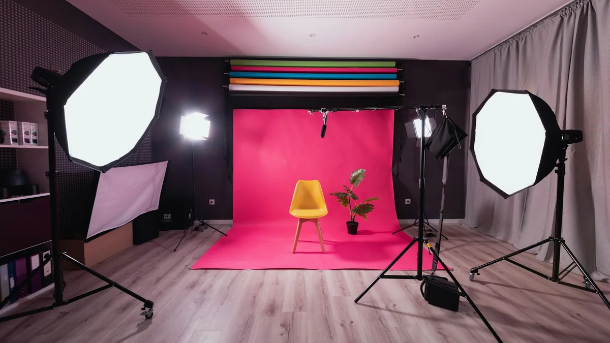 Pembe fonlu bir fotoğraf stüdyosu; ortada sarı bir sandalye, iki yanında softbox ışıklar