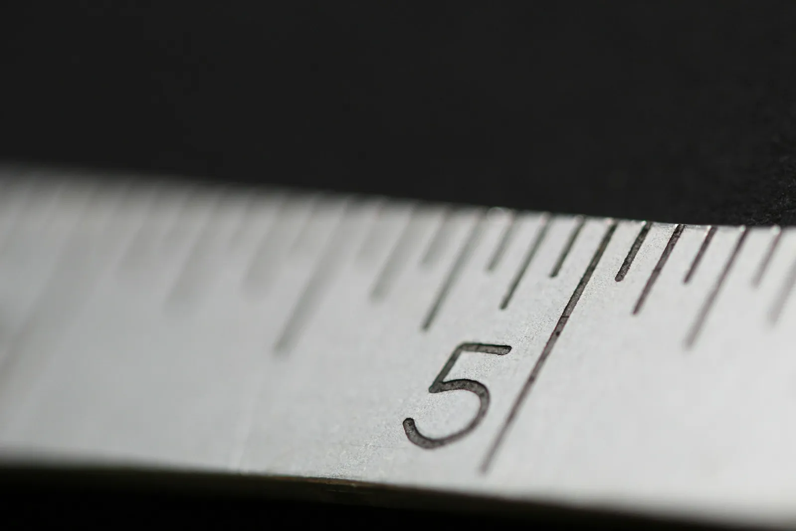 Koyu zeminde yakından çekilmiş metal bir şerit metrenin 5 rakamı ve çizgileri