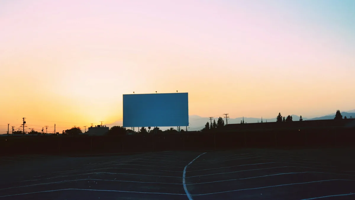 Gün batımında boş bir otoparkın ucunda duran büyük, boş bir açık hava sinema perdesi
