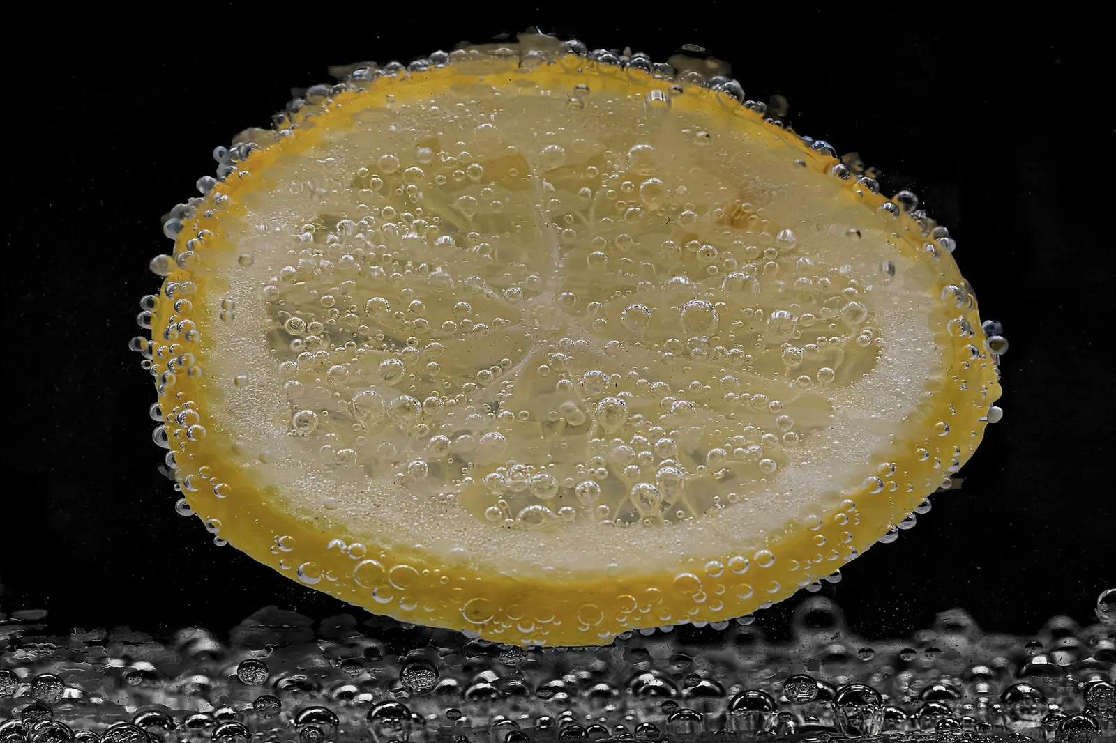 Siyah zeminde, gazlı suyun içinde kabarcıklarla kaplı bir limon dilimi
